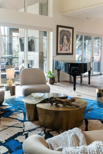 Contemporary living room featuring a black grand piano, sculptural coffee table, blue patterned rug, and floor-to-ceiling windows.