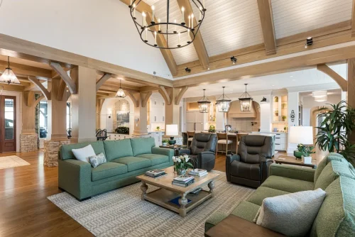 Spacious open living area with green sofas, wood beams, and a large chandelier.