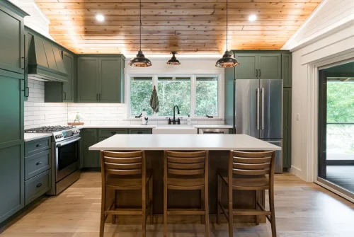 Modern kitchen with green cabinets, white island, and wood ceiling.