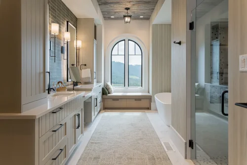 Elegant bathroom with double vanities, soaking tub, and an arched window overlooking mountains.