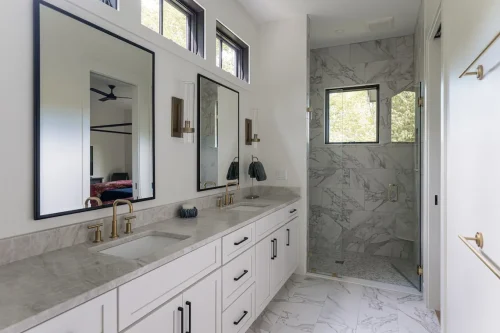 Bathroom with marble tile shower, dual vanities, and gold fixtures.