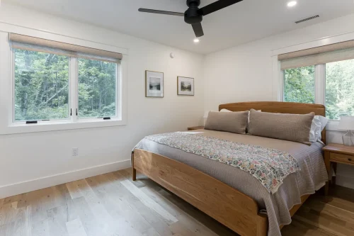 Bedroom with wood furniture and large windows overlooking trees.