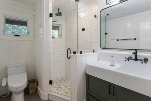 Bathroom with glass shower, white tile, and green vanity.