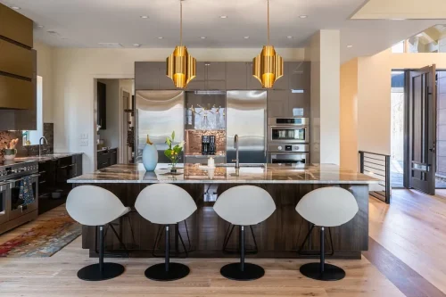 Modern kitchen with dark cabinetry, a large stone island, stainless steel appliances, and gold pendant lighting.