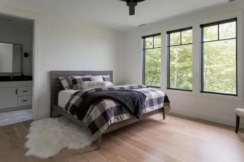 Guest bedroom with plaid bedding, sheepskin rug, and large windows.