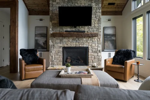 Cozy seating area with stone fireplace, leather chairs, and mounted TV.