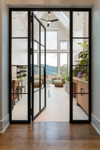 Bright sunroom with glass doors, plants, and mountain views.