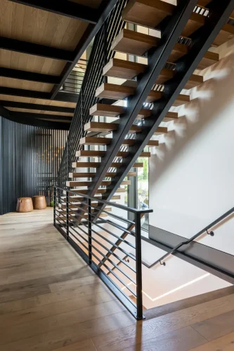 Floating wood and metal staircase with modern railing in open hallway.
