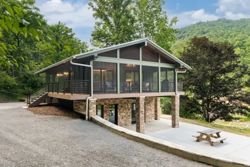 Elevated green home with screened porch and stone base.