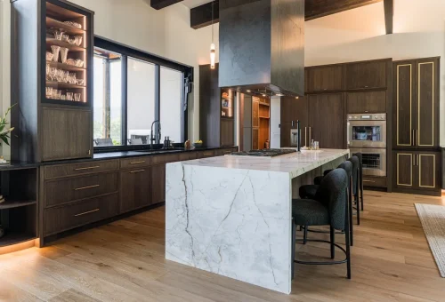 Kitchen with marble waterfall island, dark wood cabinets, and open shelving.