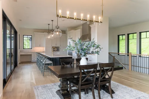 Open kitchen and dining area with white cabinetry, large island, modern lighting, and wood dining table.