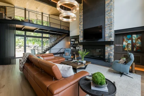 Living room with leather sectional, stone fireplace, tall ceilings, and modern chandelier.