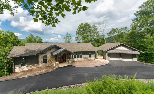 Wide view of mountain home with attached garage, stone details, and long driveway.
