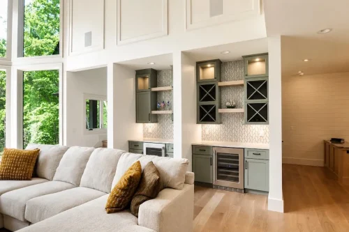 Living area with floor-to-ceiling windows and a built-in wet bar with green cabinetry, open shelving, and wine storage.