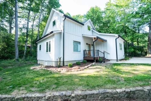 Clean-lined white home with black gutters, pitched roof, and small front porch with railing, set on a landscaped lot.