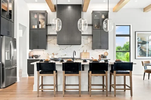 Modern kitchen with dark cabinetry, a large island with seating, glass pendant lights, and a stone backsplash.