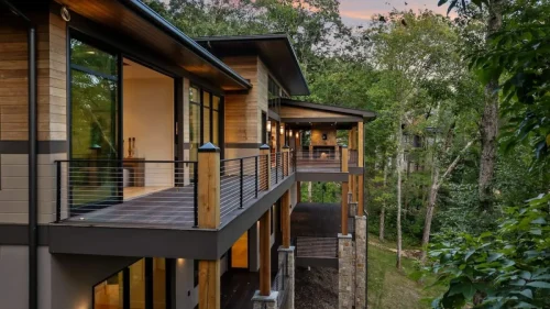 Expansive deck with wood and cable railing, covered porch with outdoor fireplace, and wooded mountain views.