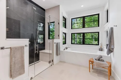 Luxury bathroom with walk-in glass shower, soaking tub, and oversized windows filling the space with natural light.