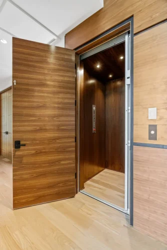 Wood-paneled residential elevator with modern controls, located just off the hallway in this custom-built home.