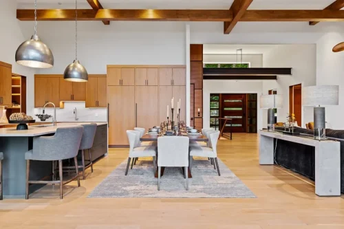 Open-concept kitchen and dining area with wood cabinetry, stone countertops, modern pendant lights, and a long dining table.