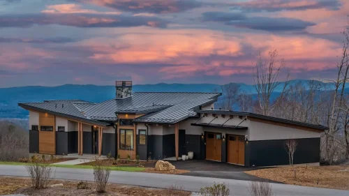 Mountain modern home with wood and dark siding exterior, lit against a dramatic sunset sky with Blue Ridge Mountains in the distance.