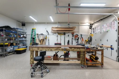 Garage workshop with a large wood workbench, tool storage, shelving, and overhead lighting.