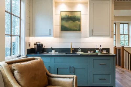 Wet bar with green cabinetry, dark countertop, brass faucet, built-in storage, and large window.