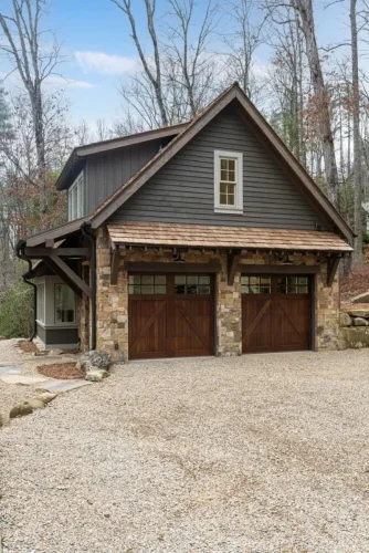 Exterior of a two-car garage with wood doors, stone siding, dark upper-level siding, and a cedar shake roof.