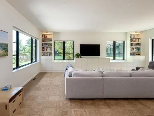 Light-filled living room with built-in cabinetry, large black-framed windows, and a sectional sofa.