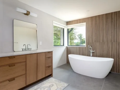Bathroom with a freestanding tub, wood vanity, vertical wood accent wall, and corner windows.