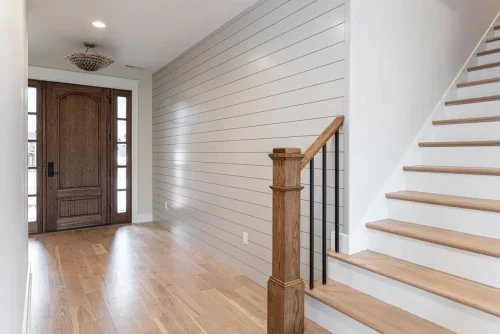 Entryway with a wood front door, hardwood floors, shiplap accent wall, and staircase with wood treads and black railings.