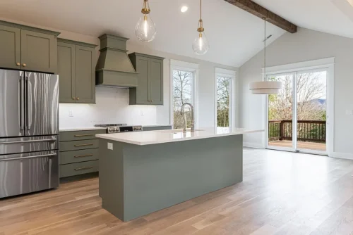 Kitchen with green cabinetry, white countertops, stainless steel appliances, a large island, and vaulted ceiling with exposed wood beam.