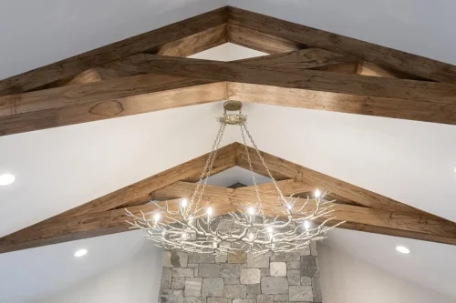 Vaulted ceiling with exposed wood trusses, a branch-style chandelier, and stone fireplace below.