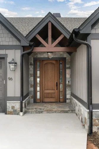 Covered front entry with a wood door, stone surround, exposed timber detail, and lantern lighting.