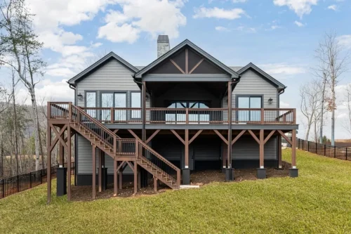 Rear exterior with an elevated covered deck, exterior staircase, wood railings, and exposed timber supports.
