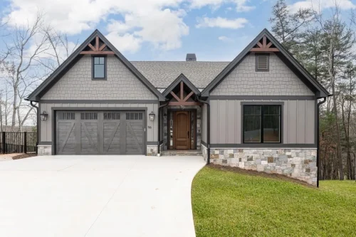 Front exterior featuring multiple gables, gray siding, stone accents, timber details, and an attached garage.