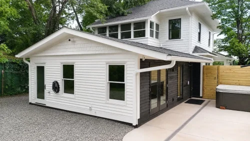 Rear exterior of a renovated white home with black accents, covered patio, gravel driveway, and fenced outdoor area.