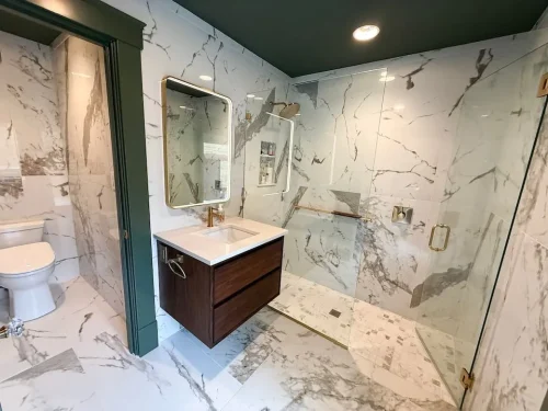 Bathroom with marble-look tile, glass walk-in shower, dark wood vanity, and brass fixtures.