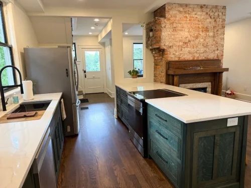 Renovated kitchen with dark cabinetry, white countertops, large island, hardwood floors, and an exposed brick fireplace.