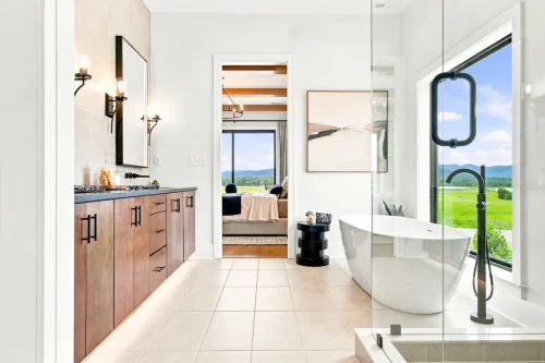 Bright bathroom with a freestanding tub, glass shower, wood vanity, black fixtures, and expansive mountain views.