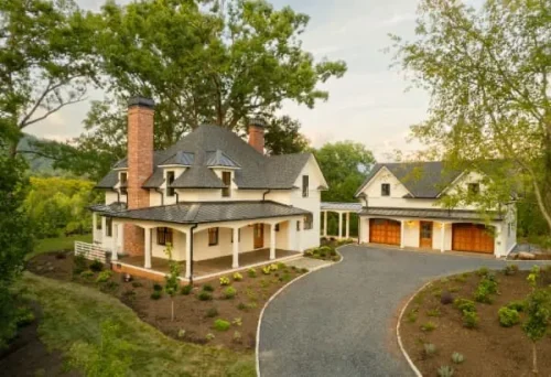 Aerial view of a white two-story home with wraparound porch, detached garage, and landscaped grounds.