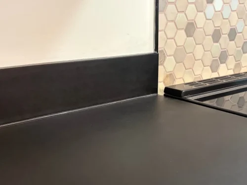 Close-up of a dark countertop and backsplash featuring multicolored hexagonal tiles beside a cooktop.