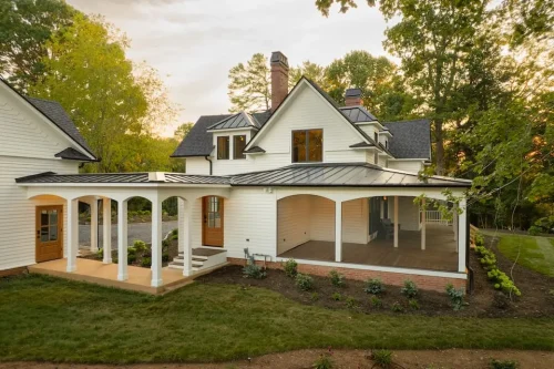 Rear view of the white two-story home with covered walkways, screened porch, landscaped lawn, and multiple gabled rooflines.