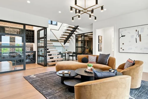 Modern sitting area with curved seating, an open staircase, glass-enclosed wine storage, and an adjoining exercise room.