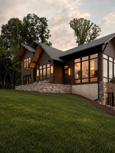 Side view of a contemporary mountain home with wood siding, expansive black-framed windows, stonework, and a terrace