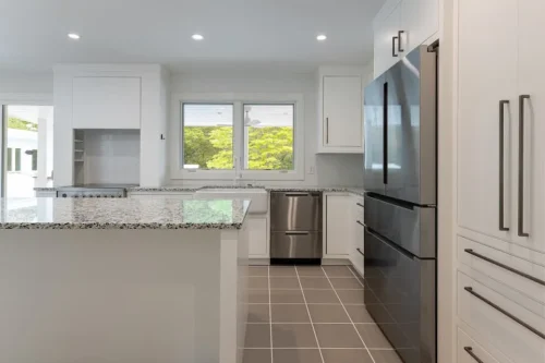Renovated kitchen with white cabinetry, stone countertops, stainless steel appliances, and large island.
