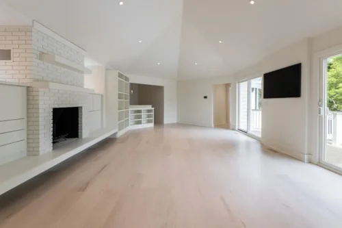 Renovated living room with vaulted ceiling, light wood flooring, white brick fireplace, built-in shelving, and sliding glass doors.