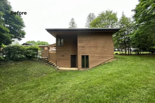 Before renovation side exterior with brown wood siding, lower-level doors, and grassy yard.