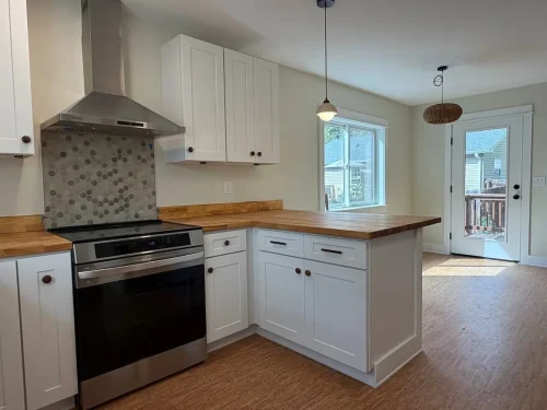 Kitchen and dining area featuring white cabinetry, butcher block countertops, a stainless steel range, hexagonal tile backsplash, and natural light.
