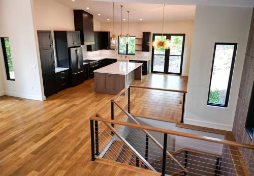 Inside of the Tulip Poplar home; WNC Parade of Homes; Modern Home view of open layout, focus on kitchen with black cabinets, and white tile backsplash. Big island in center of kitchen and open space for table.